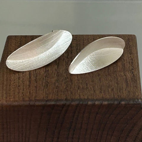 Two silver oval earrings on a wooden surface