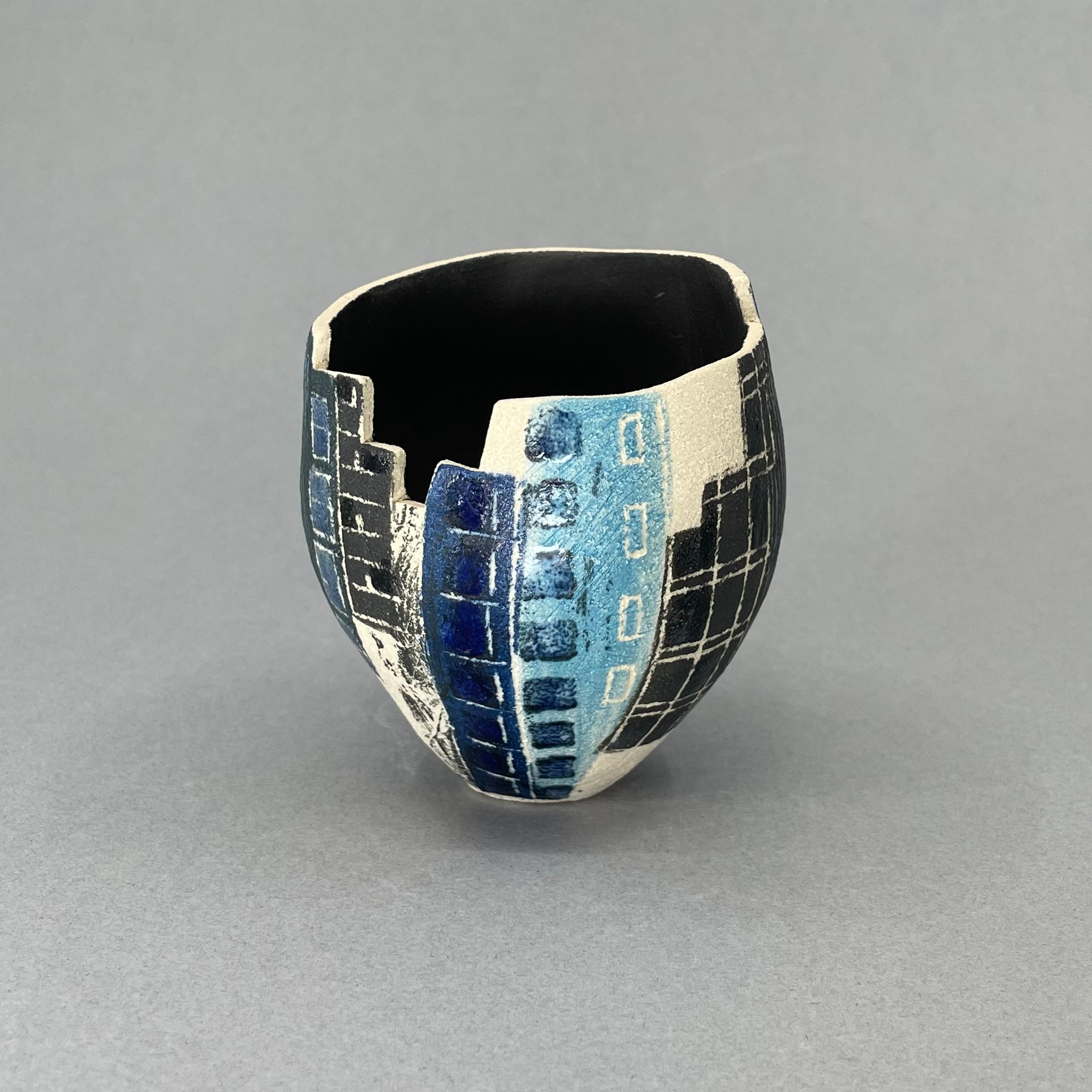 Inspired by a trip to Ground Zero in New York. Linda has hand-built this piece using white stoneware and decorated with slips and underglazes. Linda uses various techniques including Sgraffito, inlay and printing to create her architectural collection.  This piece measures approximately 9cm high and 7cm in diameter.Small New York Vessel