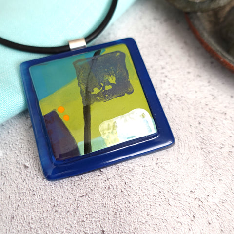 Square square pendant on  a rubber necklace Bright green, navy and white design on a navy background. 5 x 5cm