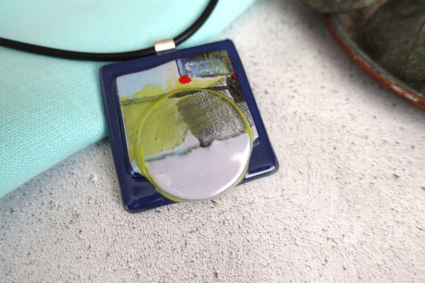 5cm square fused glass pendant in three layers, hand painted with enamels in an abstract pattern of lime, navy and blue. Sterling silver bail 