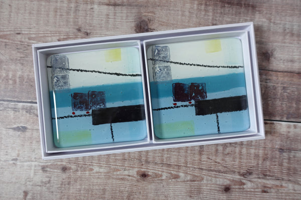 Spring tide Coaster set by jenny Hoole. A mix of ocean blue abstract shapes on a lighter background with soft yellow highlights. 10cm x 10cm with bumper feet.