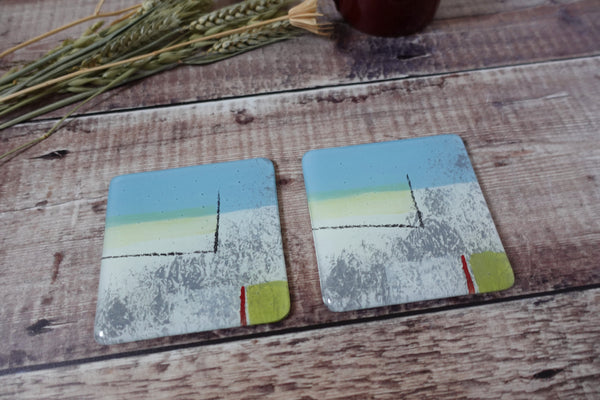 Summer Breeze Coaster Set by Jenny Hoole. 10cm square coasters with bumper feet to protect furniture. Fused glass with an enamel seaside  design in abstract shapes with highlights of soft yellow and grey.