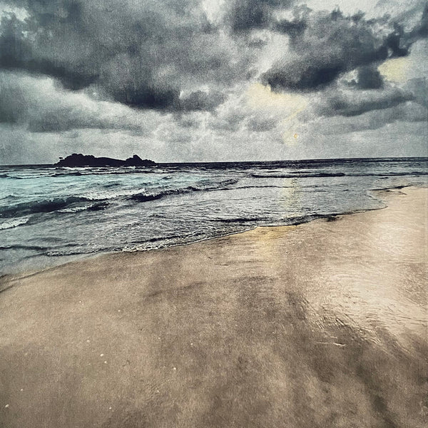 Photoetching of a sandy beach and a little island on the left; the sand is sandy colour, the sea is a tonal blue and the sky is grey blue