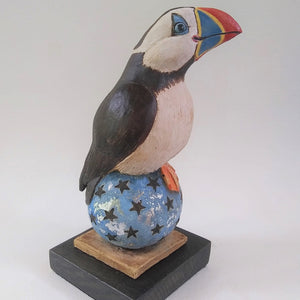 A charming sculpture of  a Puffin Standing on a starry ball, highlighted with silver leaf